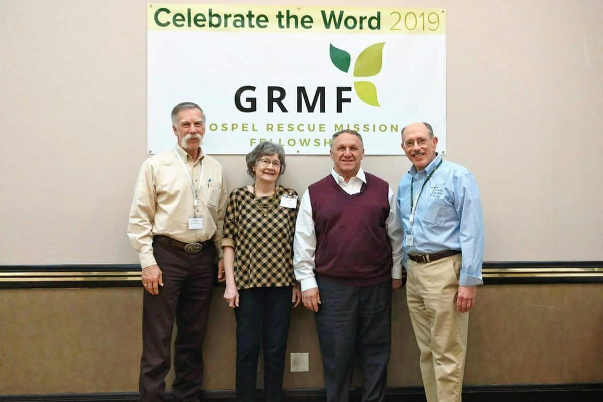 Four members of the first GRMF Board of Directors in front of a "Celebrate the Word 2019" banner