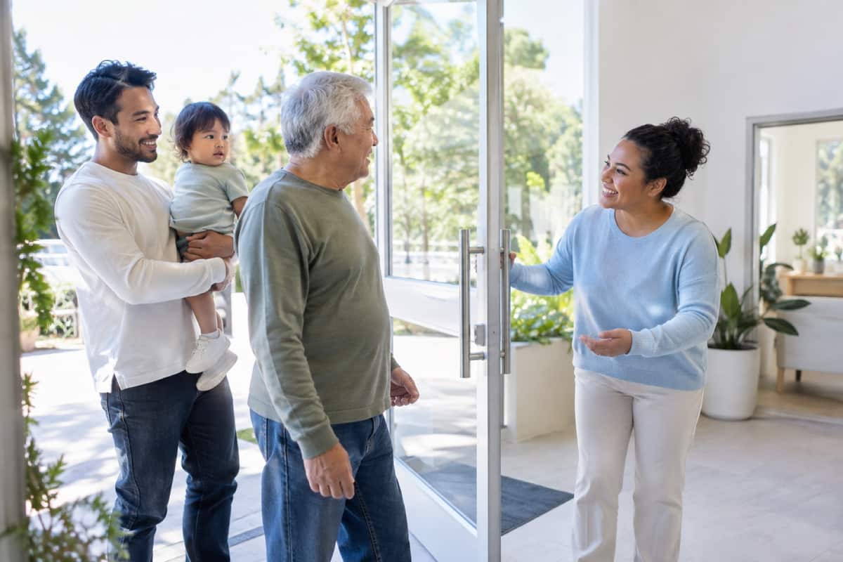 A volunteer welcoming a family at the door of a sunny community center